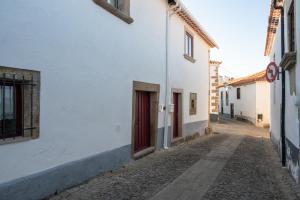 an alley with a white building and a red door at Portas da Villa in Miranda do Douro
