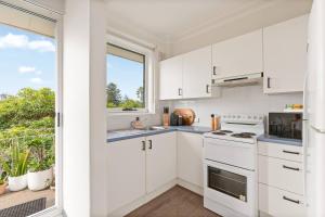 a kitchen with white cabinets and a window at Shoreleaf Haven - Moments from Waves & Seaside Eats in Deewhy +8 photos