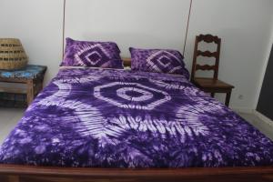 a purple comforter on a bed with a chair at Campement Emanaye in Oussouye