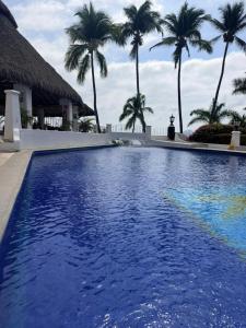 a large blue swimming pool with palm trees in the background at Frente al mar, comodo y familiar en Playasol Manzanillo in Manzanillo
