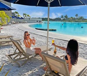 two women sitting in chairs on a beach with drinks at kristal lagoon view apartement in Cartagena de Indias