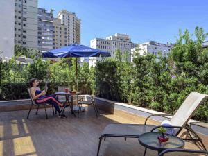 a woman sitting at a table with an umbrella on a rooftop at Mercure Sao Paulo Jardins in São Paulo