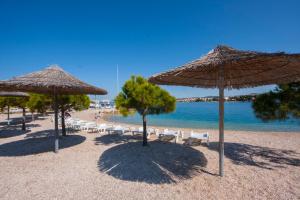 a beach with umbrellas and chairs and the water at Apartments Beader in Brodarica