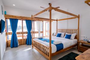 a bedroom with a wooden canopy bed with blue curtains at Dhanrains La Rocha in Patnem