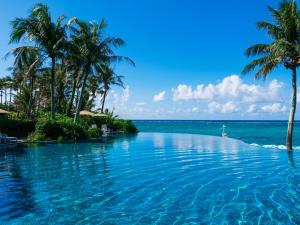 a swimming pool next to the ocean with palm trees at HOTEL MOON BEACH MUSEUM RESORT in Onna