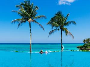 a person in a paddle board on a beach with two palm trees at HOTEL MOON BEACH MUSEUM RESORT in Onna
