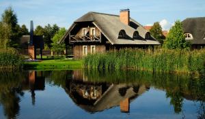 uma casa com um telhado de palha refletindo na água em Pajūrio Sodyba em Šventoji