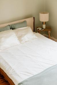 a bed with white sheets and a lamp on a table at Katrina Summer House in Jūrmalciems