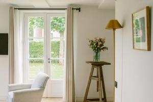 ein Wohnzimmer mit einem Fenster, einem Stuhl und einer Vase mit Blumen in der Unterkunft Domaine de Primard - Fontenille Collection in Guainville