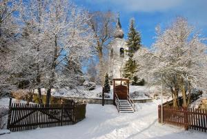 a church covered in snow with a gate and a fence at Füstös Cottage Gömörszőlős in Gömörszőlős