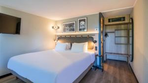 a bedroom with a large bed with white sheets at Campanile NATURE - Strasbourg Sud Geispolsheim in Geispolsheim