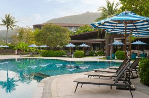 ein Swimmingpool mit Liegestühlen und einem Sonnenschirm in der Unterkunft OZO Phuket in Kata Beach