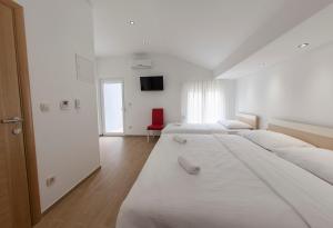 a white room with three beds and a red chair at Villa Klara Guest House in Baška Voda