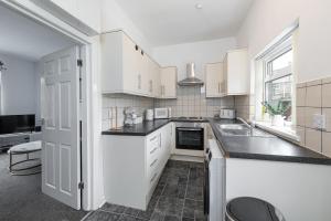 a kitchen with white cabinets and a black counter top at The Cosy Durham Nest in Langley Park +16 photos
