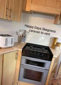 a kitchen with a stove and a sign that says happy daysessen caravan to rent at 6 berth static in Skegness in Chapel Saint Leonards +7 photos