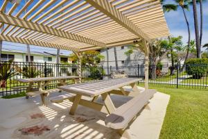 a picnic table and benches under a wooden pergola at Lanai & Community Pool Access: Sunny Central Condo in Kailua-Kona