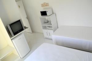 a small white room with a bed and a tv at Hospedaria Canto do Morro in Bombinhas