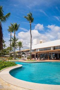 a swimming pool with palm trees and a building at Arraial D'ajuda Eco Resort in Arraial d'Ajuda