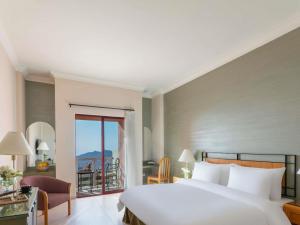a bedroom with a large white bed and a balcony at Grand Mercure Petra in Wadi Musa