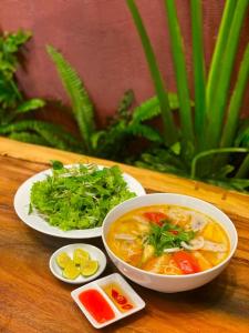 a table with a bowl of soup and plates of greens at Luu Ngai Condotel Quy Nhon in Quy Nhon