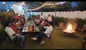 a group of people sitting around a table with a fire at Aacasa Living Resorts in Shamshabad