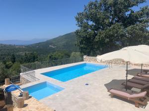 a swimming pool with an umbrella and chairs and a swimming poolvisor at Kouvarata Villas Stavros in Vathi
