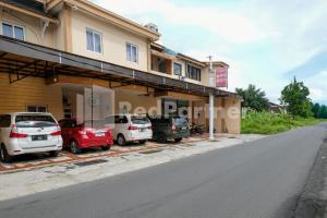 a building with cars parked in front of a street at Aster Triplets Guest House JCM Mitra RedDoorz in Yogyakarta