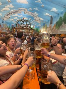 a group of people holding up glasses of beer at Beer Base-Camp Oktoberfest camping with free welcome beer and traditional dirndl-lederhosen shop in Munich
