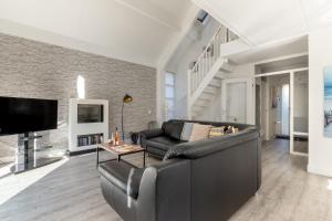 a living room with a black leather couch and a tv at Villa Beach & Spa in Julianadorp