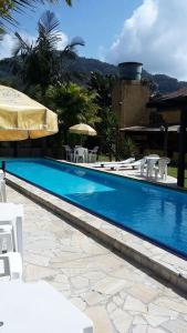 a swimming pool with white chairs and an umbrella at Pousada Lugar Comum in Boicucanga