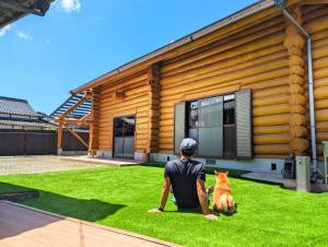 a man and a dog sitting on the grass in front of a house at Loghouse HOKA -バレルサウナ付貸切別荘 大型犬ペット可 in Kama