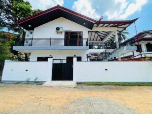 a white house with a black gate and white fence at Vihen Homestay in Dickwella