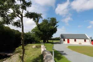 a white barn with a tree next to a road at Historic Louisburgh Farm Cottage in Louisburgh