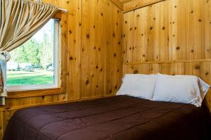 a bedroom with wooden walls and a bed with a window at Yosemite Lakes Cabin & Cottages in Harden Flat