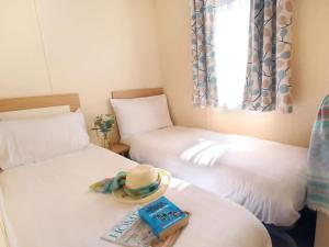 a room with two beds with a hat and a book at 1. Forest Edge 2 Bedroom Statement Caravan in Saint Leonards