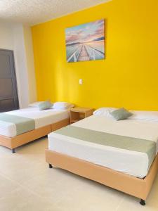 two beds in a room with a yellow wall at HOTEL CATALUÑA PEREIRa in Pereira