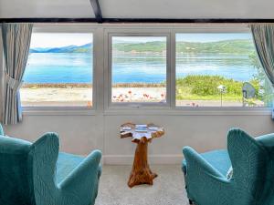 a living room with two chairs and a table and two windows at The Heron in Ardentinny