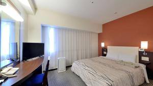 a bedroom with a bed and a desk with a television at Takaoka Manten Hotel Ekimae in Takaoka