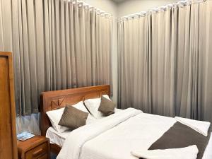 a bedroom with a bed with white sheets and gray drapes at Valensa lake view in Kalpetta