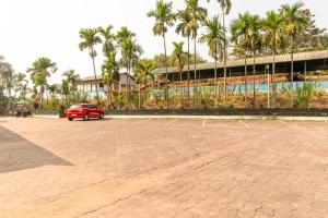 a red car parked in a parking lot with palm trees at Treebo Pratham Inn Water Park Resort With Swimming Pool in Kundapur +52 photos