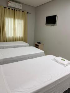 a room with two beds and a tv on the wall at Plaza Hotel in Mineiros