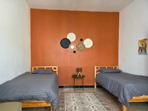 two beds in a room with an orange wall at Les Sables Bleus in Le Kram