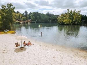 a group of people sitting on a beach with an umbrella at Camping Etang de Sologne in Nouan-le-Fuzelier +30 photos