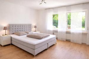 a white bedroom with a bed and two windows at Ferienwohnung Westerwaldblick großzügige Wohlfühloase mit Terrasse in Oberelbert