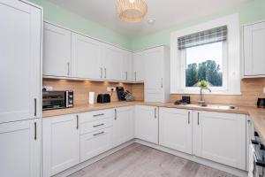 a white kitchen with white cabinets and a window at Ideal Work Stays 3BR 6 Guests Free Parking in Falkirk