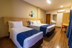 a hotel room with two beds and a desk at Luds Comfort Hotel in Ponta Grossa