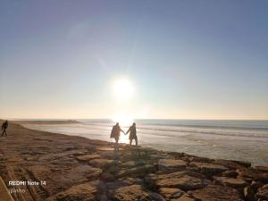 two people walking on the beach with the sun in the background at Aurora do Furadouro II in Ovar
