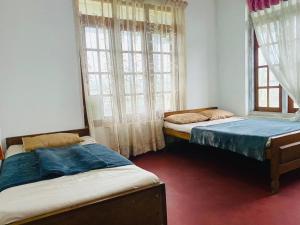 two beds in a room with two windows at Siloneeds HOSTEL in Nuwara Eliya