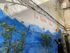 a man painting a blue wall with writing on it at La Kasbah Salam Hostel in Fez