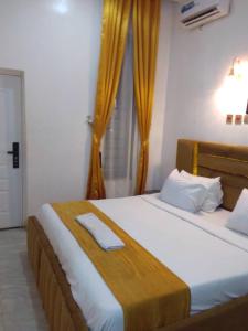 a bedroom with a large white bed with yellow curtains at White Angel Hotel Kubwa in Kubwa